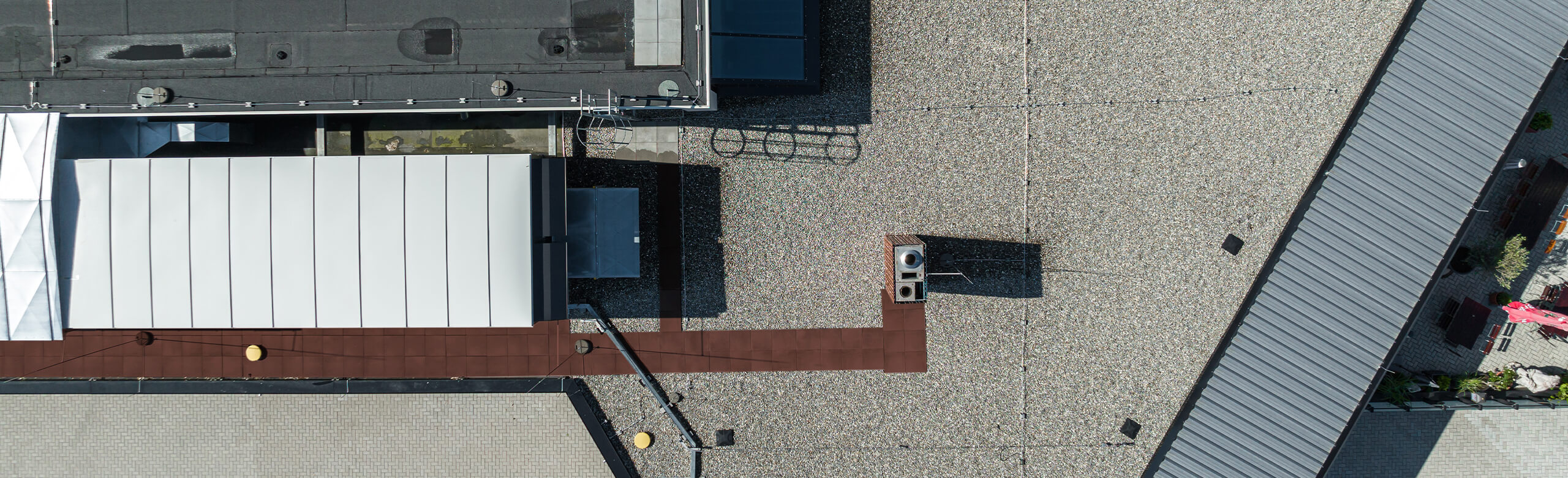Construction – Solutions pour toitures plates et zones de toiture sûres Vue aérienne d’un toit plat avec gravillons, équipements techniques et chemin de maintenance; texte « Construction »
